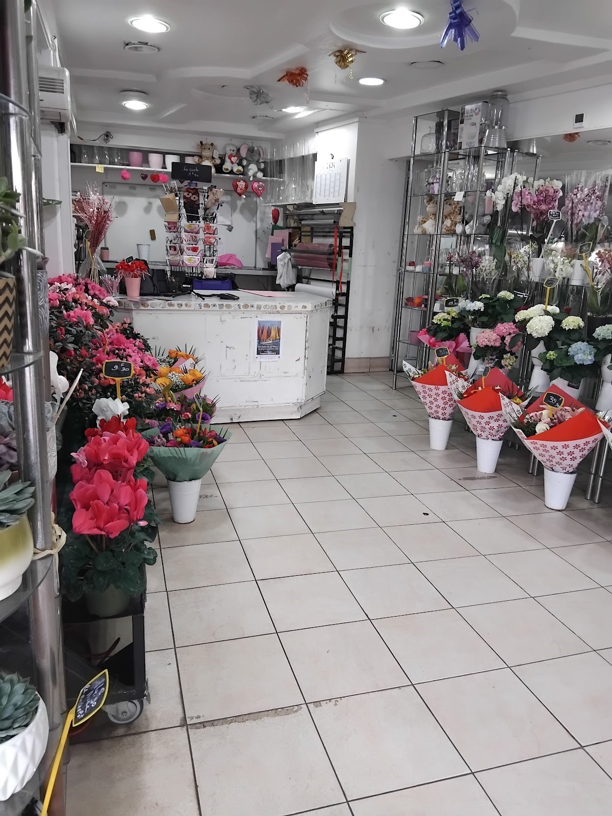 L’intérieur de la boutique&nbsp;: comptoir blanc, bouquets emballés de rouge et de rose, orchidées